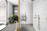 This luxurious bathroom boasts a spacious walk-in shower with sleek gold fixtures and subway tiles, complemented by a freestanding bathtub with a gold faucet.