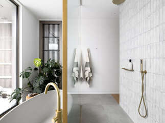 This luxurious bathroom boasts a spacious walk-in shower with sleek gold fixtures and subway tiles, complemented by a freestanding bathtub with a gold faucet.