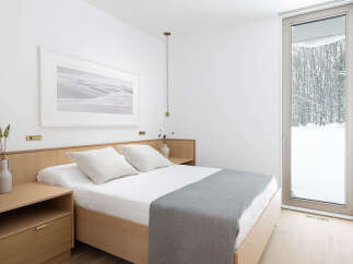 This minimalist bedroom boasts a light and airy feel, featuring a light wood platform bed with crisp white linens and a gray throw.