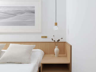 This serene bedroom boasts a minimalist aesthetic with a light oak wood headboard and nightstand, complemented by crisp white linens and a monochrome desert landscape print.