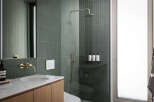 This modern bathroom boasts sleek, dark green tiles, gold-toned fixtures, and a frameless glass shower enclosure.