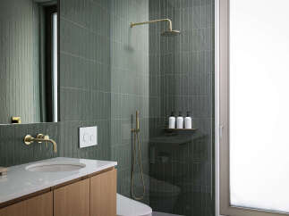 This modern bathroom boasts sleek, dark green tiles, gold-toned fixtures, and a frameless glass shower enclosure.