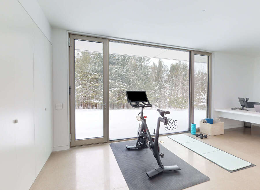 This stunning home gym boasts floor-to-ceiling windows showcasing a breathtaking snowy landscape, creating a serene and inspiring workout environment.