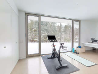 This stunning home gym boasts floor-to-ceiling windows showcasing a breathtaking snowy landscape, creating a serene and inspiring workout environment.