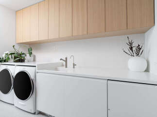 This laundry room boasts a clean, modern design with white cabinetry and countertops, complemented by light wood upper cabinets.