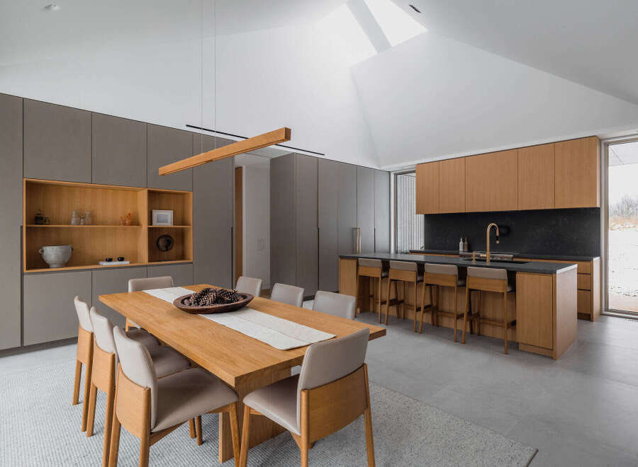 This stunning modern kitchen boasts a spacious island with bar seating, sleek gray and light wood cabinetry, and a large window offering scenic views.