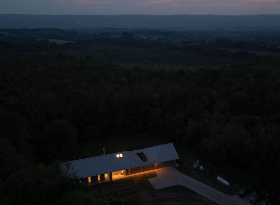 Nestled in a verdant forest, this modern home boasts a sleek, metal roof and energy-efficient design, as evidenced by the visible charging station.