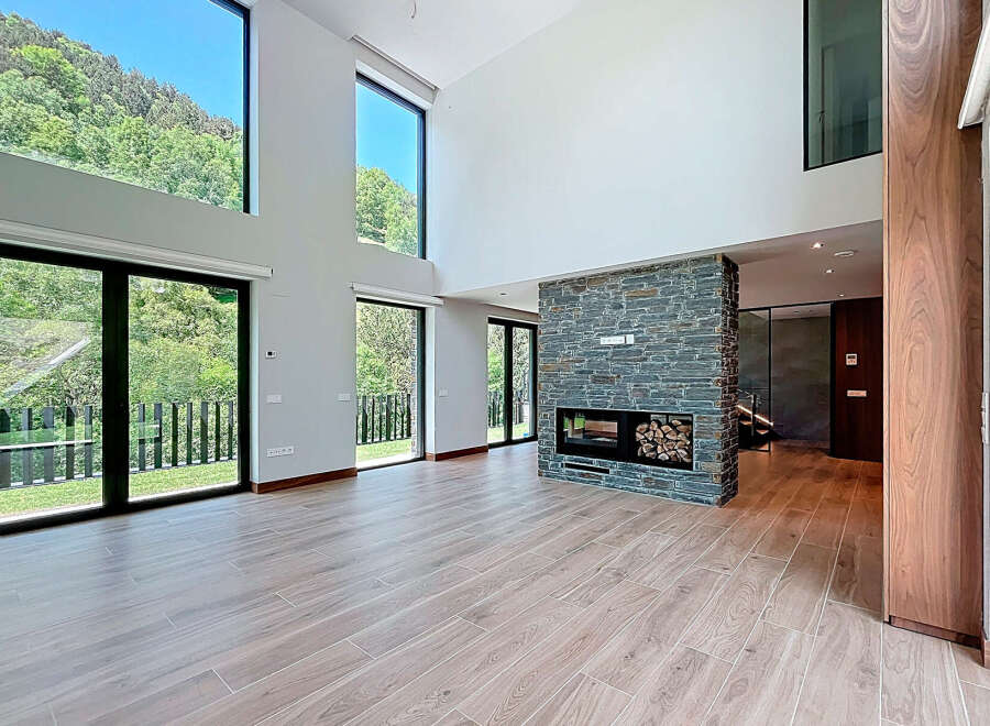 This modern living room features a striking stone fireplace, wood-look tile flooring, and expansive windows offering stunning views.