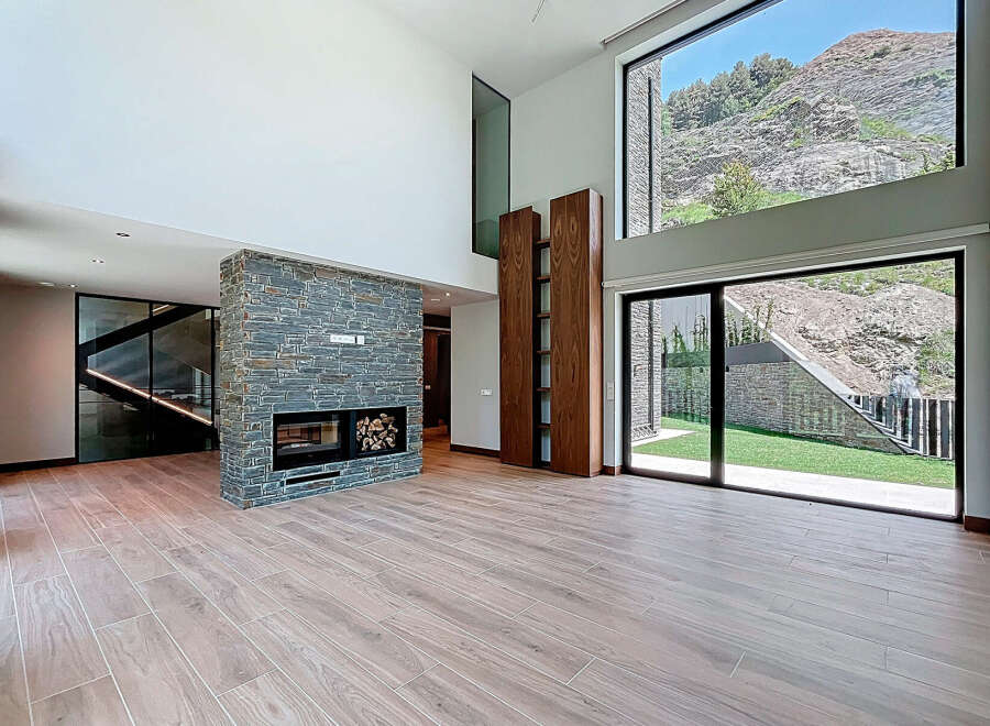 This stunning modern living room features a striking stone fireplace and expansive windows showcasing breathtaking mountain views.