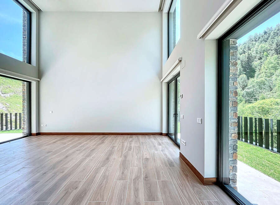This modern living room features an open floor plan, light wood floors, and expansive windows that offer stunning nature views.