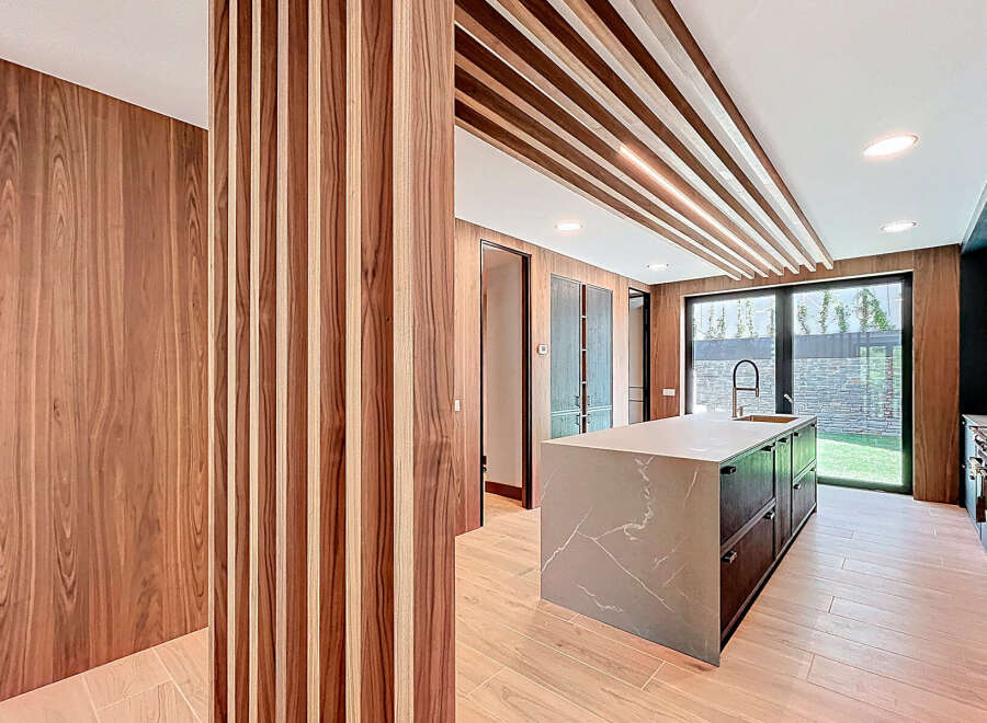 This modern kitchen features sleek wood paneling, a striking marble-topped island, and a unique slatted ceiling design.