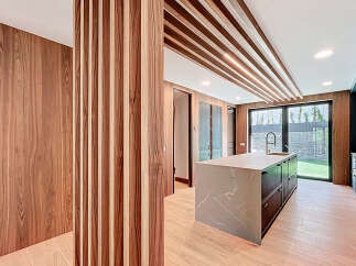 This modern kitchen features sleek wood paneling, a striking marble-topped island, and a unique slatted ceiling design.
