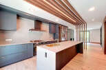 This modern kitchen features sleek gray cabinetry, a large central island with a gold sink, and a unique wooden slat ceiling design with integrated lighting.