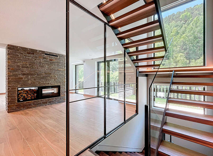 This modern home boasts a stunning staircase design with wooden steps and a glass railing, creating an open and airy feel.