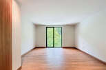 This bright, empty room features wood-look tile flooring and a large glass door offering views of lush greenery.