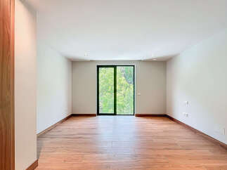 This bright, empty room features wood-look tile flooring and a large glass door offering views of lush greenery.