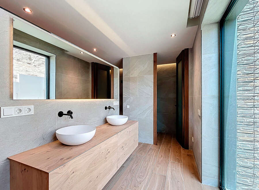 This modern bathroom features a double sink vanity with sleek black faucets, complemented by a large mirror and natural wood accents.