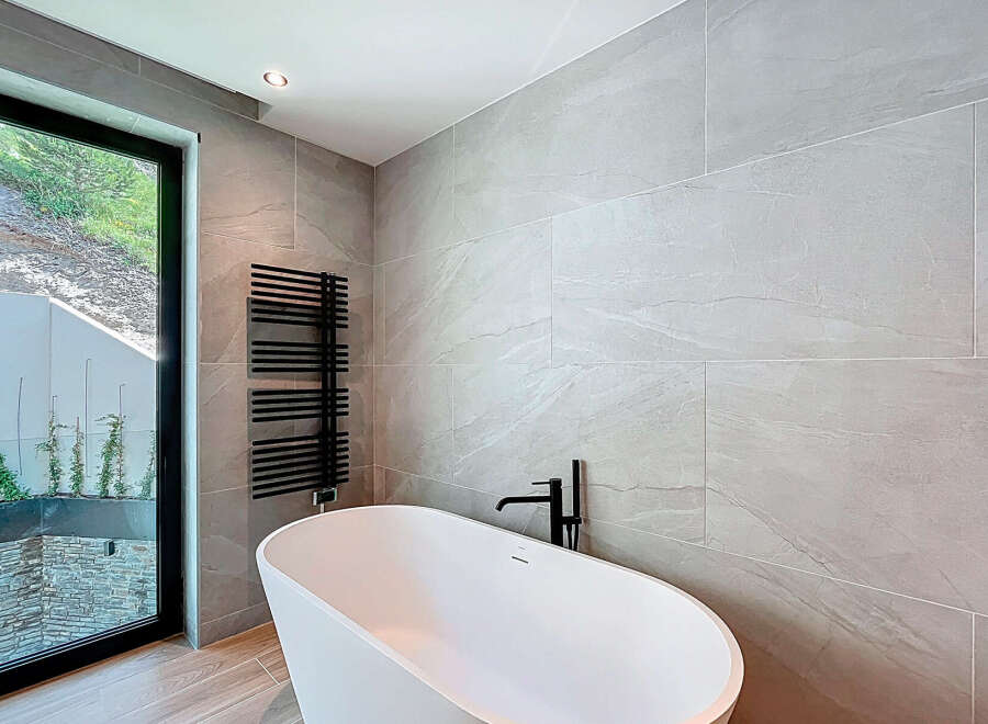This modern bathroom boasts a sleek, freestanding white bathtub paired with a stylish black faucet and towel warmer.