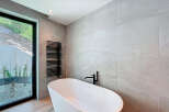 This modern bathroom boasts a sleek, freestanding white bathtub paired with a stylish black faucet and towel warmer.