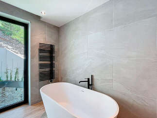 This modern bathroom boasts a sleek, freestanding white bathtub paired with a stylish black faucet and towel warmer.