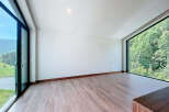 An expansive room features wood-look tile flooring and a natural wood baseboard, complemented by large windows that offer stunning views of the surrounding greenery.