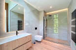 This modern bathroom features sleek gray tiles, a wood-paneled vanity with a minimalist sink, and a glass-enclosed shower.