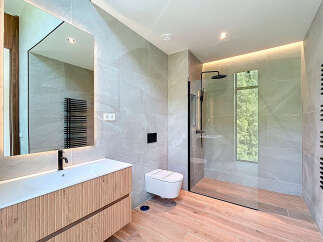 This modern bathroom features sleek gray tiles, a wood-paneled vanity with a minimalist sink, and a glass-enclosed shower.