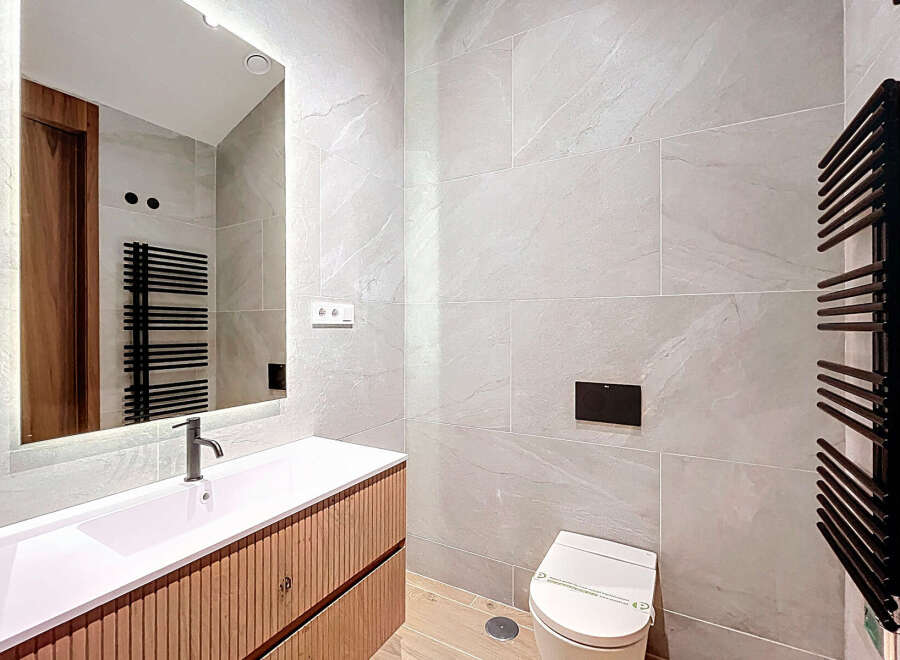 This modern bathroom features a sleek, integrated sink and vanity with a light wood finish, complemented by large-format grey marble-effect tiles.