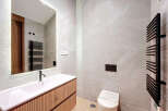 This modern bathroom features a sleek, integrated sink and vanity with a light wood finish, complemented by large-format grey marble-effect tiles.
