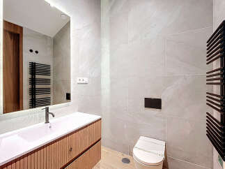 This modern bathroom features a sleek, integrated sink and vanity with a light wood finish, complemented by large-format grey marble-effect tiles.