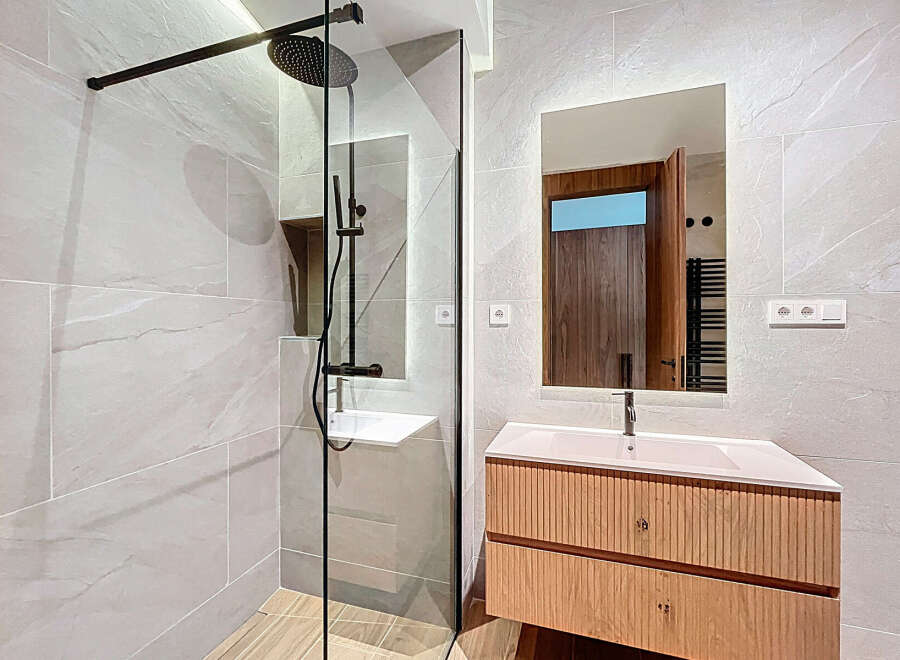 This modern bathroom features a sleek, glass-enclosed shower with black fixtures, complemented by a stylish vanity with a light wood finish.