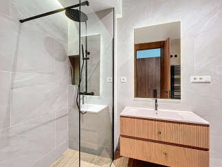 This modern bathroom features a sleek, glass-enclosed shower with black fixtures, complemented by a stylish vanity with a light wood finish.