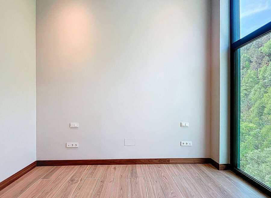 This is an empty room with hardwood floors, light gray walls, and modern dark wood trim.