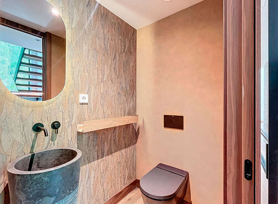 This modern powder room features unique design elements, including a stone vessel sink with matte black fixtures and a sleek toilet.