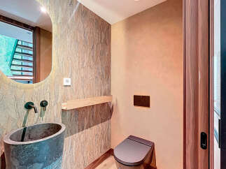This modern powder room features unique design elements, including a stone vessel sink with matte black fixtures and a sleek toilet.