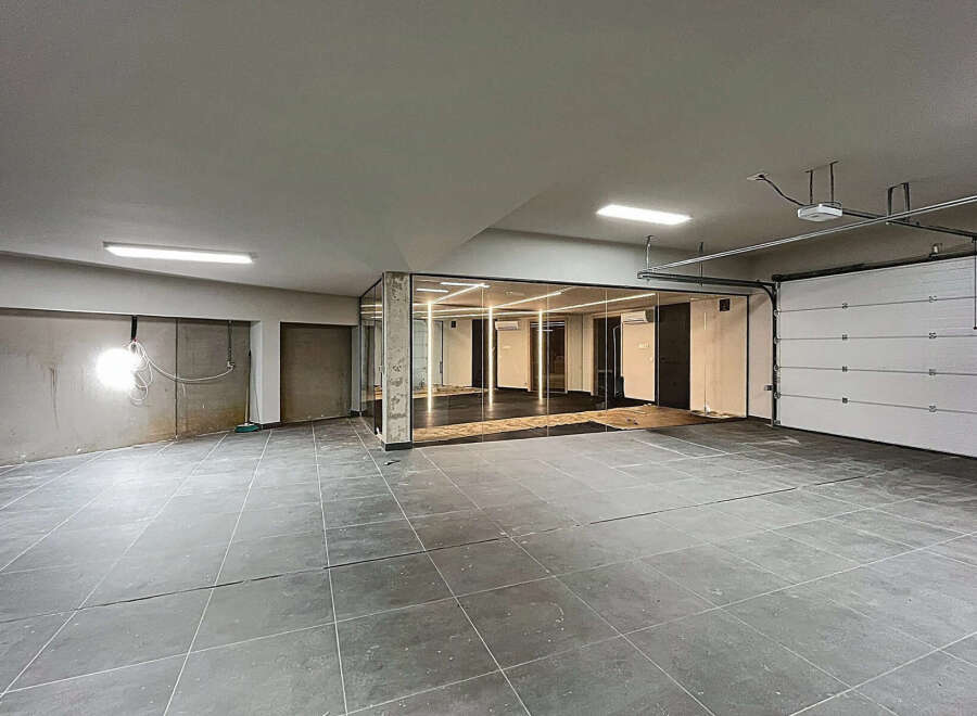 Discover this versatile commercial space featuring an open layout with modern tile flooring, a sleek glass-enclosed office area, and convenient garage door access.