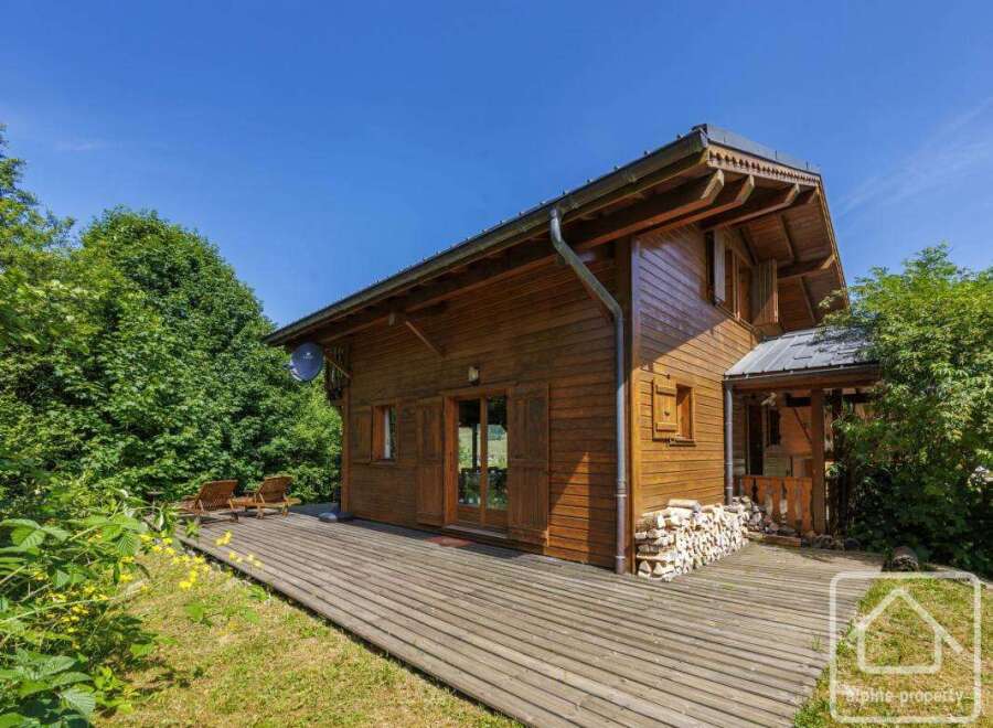 A charming wooden chalet nestled in a lush green landscape with a spacious wooden deck.