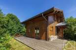 A charming wooden chalet nestled in a lush green landscape with a spacious wooden deck.