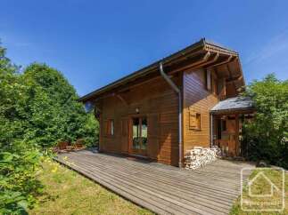 A charming wooden chalet nestled in a lush green landscape with a spacious wooden deck.