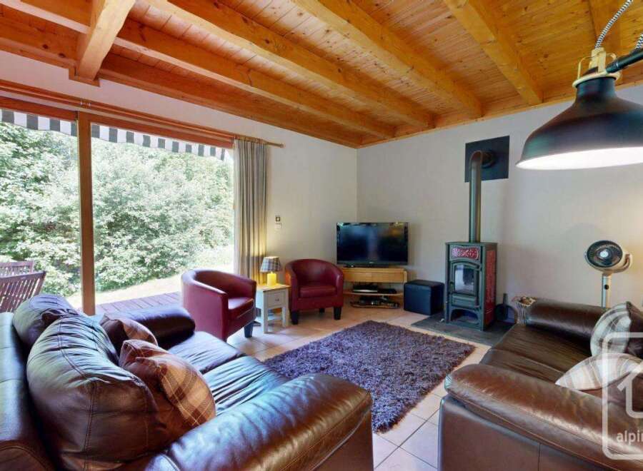 A cozy living room showcases a rustic wood-beamed ceiling and plush leather seating, complemented by a classic wood-burning stove.
