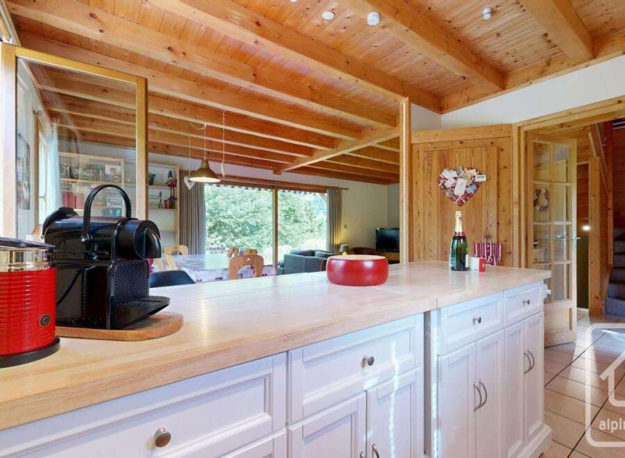 This kitchen features a bright and airy space with white cabinets, light wood countertops, and a rustic wood ceiling.