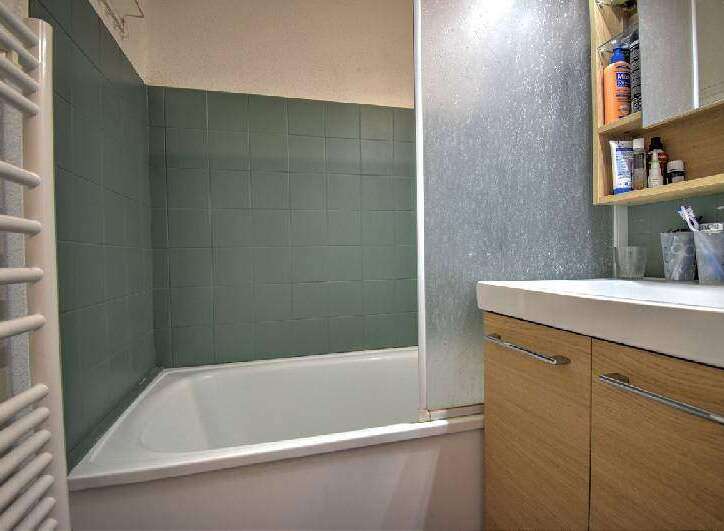 This bathroom features a bathtub with green tile surround and a modern wood vanity.