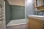 This bathroom features a bathtub with green tile surround and a modern wood vanity.