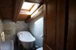 This bathroom boasts a rustic charm with its wood-paneled ceiling and exposed beams, complemented by a skylight that floods the space with natural light.
