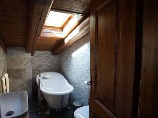 This bathroom boasts a rustic charm with its wood-paneled ceiling and exposed beams, complemented by a skylight that floods the space with natural light.