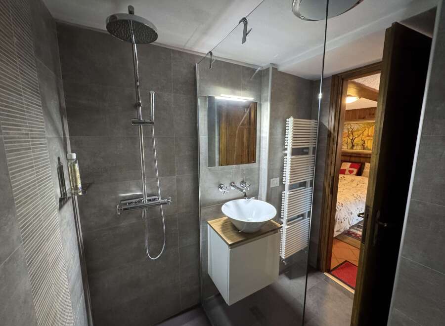 This modern bathroom features sleek gray tiling, a stylish vessel sink on a minimalist vanity, and a contemporary shower system.