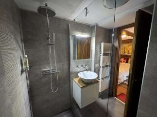 This modern bathroom features sleek gray tiling, a stylish vessel sink on a minimalist vanity, and a contemporary shower system.