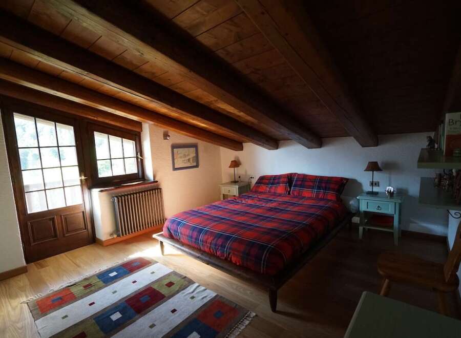 Charming bedroom featuring exposed wooden beams, a cozy plaid comforter, and natural light streaming through the windows, creating a warm and inviting atmosphere.