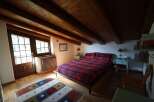 Charming bedroom featuring exposed wooden beams, a cozy plaid comforter, and natural light streaming through the windows, creating a warm and inviting atmosphere.