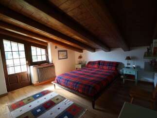 Charming bedroom featuring exposed wooden beams, a cozy plaid comforter, and natural light streaming through the windows, creating a warm and inviting atmosphere.